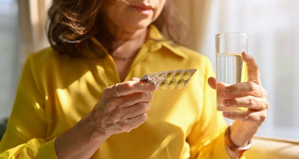 Frau, hält einen Blister mit Tabletten und ein Glas Wasser in der Hand.