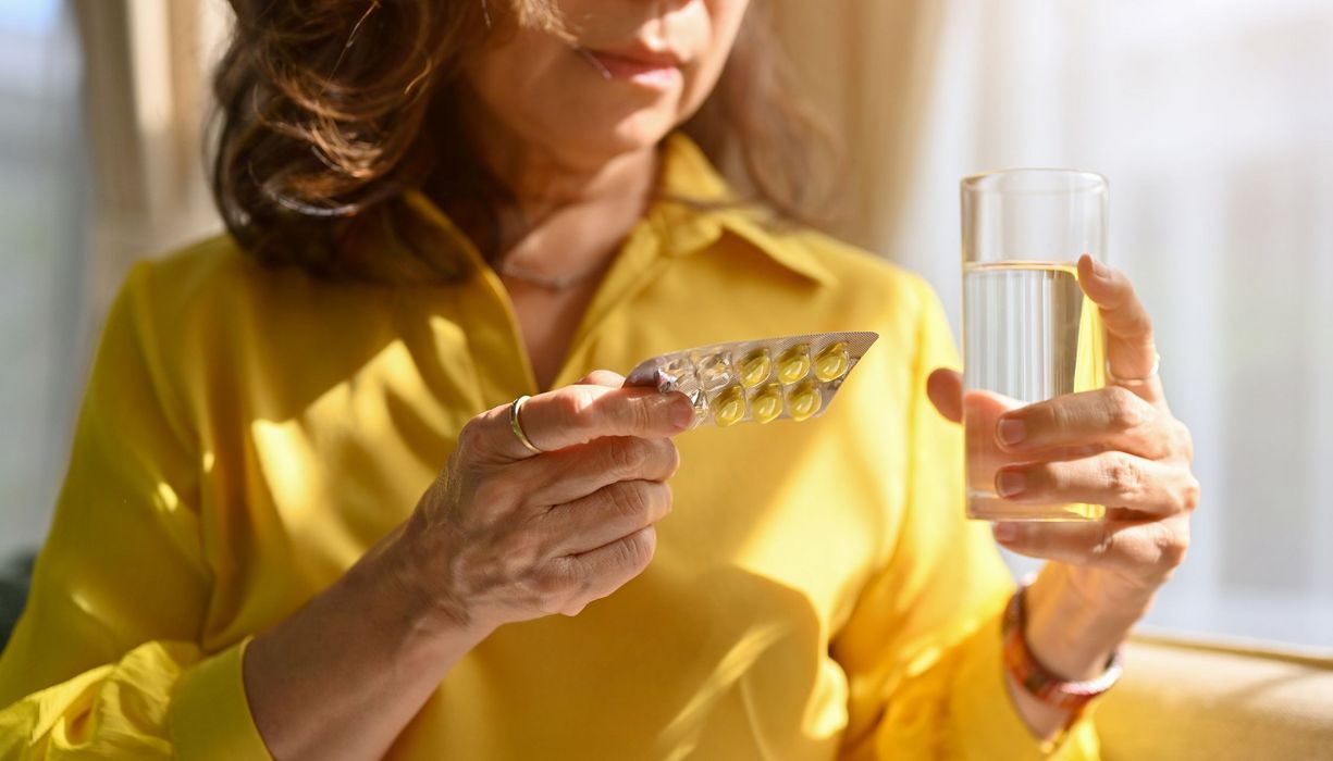 Frau, hält einen Blister mit Tabletten und ein Glas Wasser in der Hand.