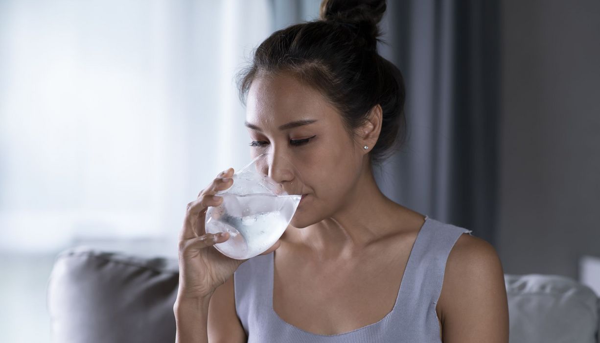 Junge Frau, trinkt Wasser mit Eiswürfeln.
