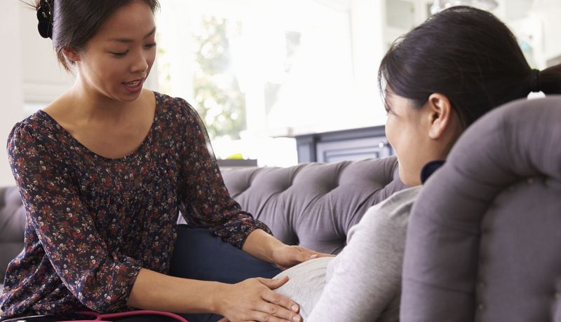 Eine Hebamme untersucht den schwangeren Bauch einer Patientin bei ihr zuhause.