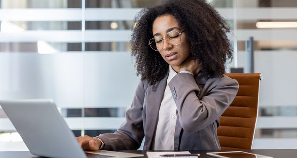 Junge Frau im Büro legt sich die Hand in den Nacken.