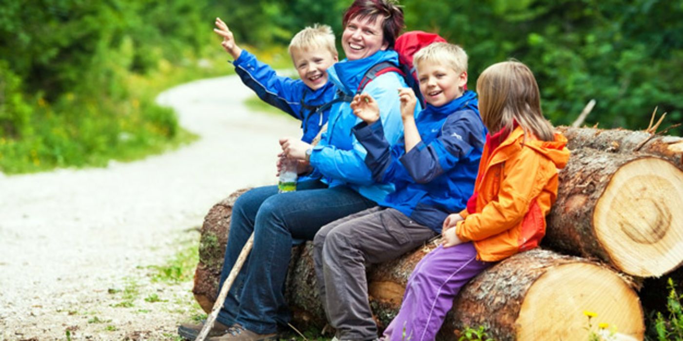 Fröhliche Familie in Wanderkleidung sitzt auf einem großen Baumstamm im Wald
