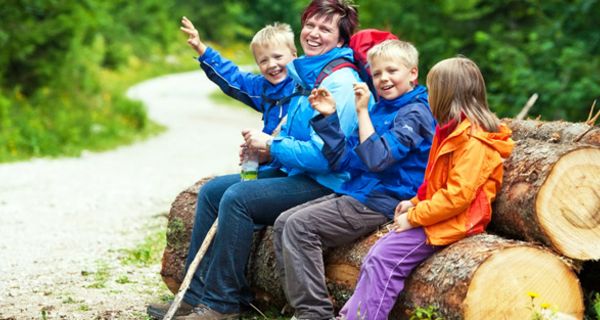 Fröhliche Familie in Wanderkleidung sitzt auf einem großen Baumstamm im Wald