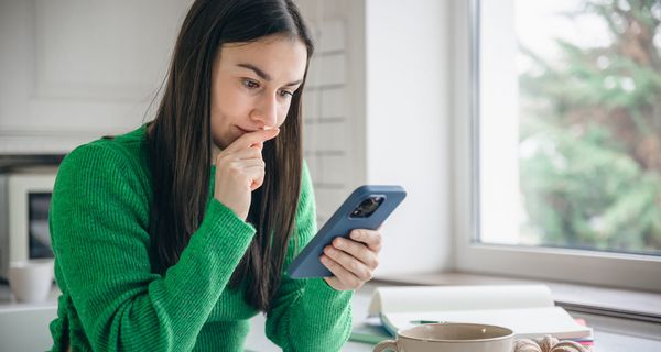 Junge Frau, schaut nachdenklich ins Smartphone.