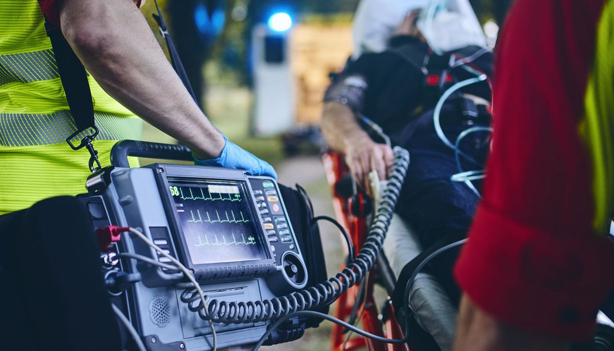 Ein Team Sanitäter bringt einen Patienten, der an ein Herzfrequenzmesser angeschlossen ist, zum Krankenwagen.