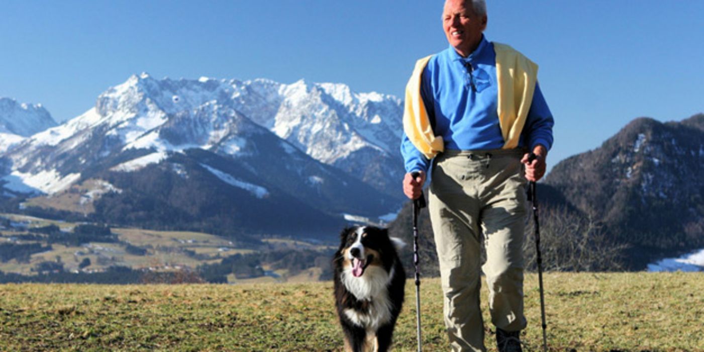 Senior mit Hund beim Nordic Walking in den Bergen.