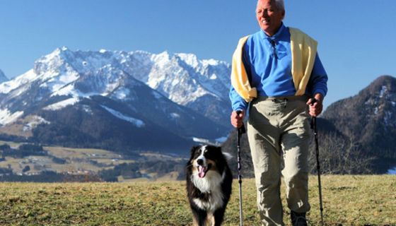 Senior mit Hund beim Nordic Walking in den Bergen.
