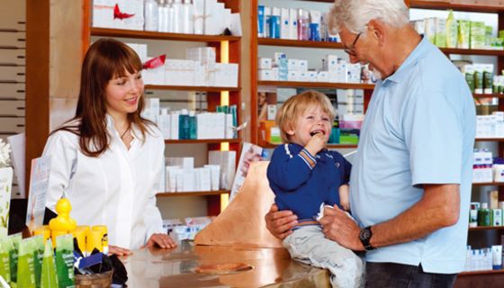 Älterer Mann mit seinem Enkel im Gespräch mit einer Apothekerin