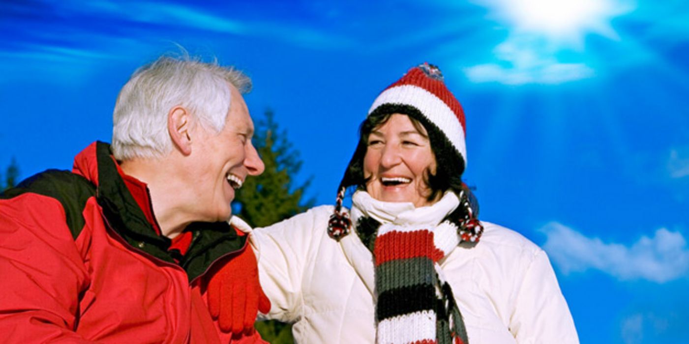 Lachendes älteres Paar in sportlicher Kleidung vor Wintersonnenhimmel