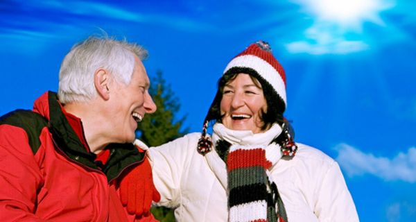 Lachendes älteres Paar in sportlicher Kleidung vor Wintersonnenhimmel