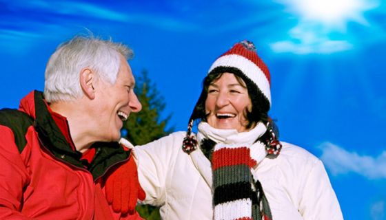 Lachendes älteres Paar in sportlicher Kleidung vor Wintersonnenhimmel