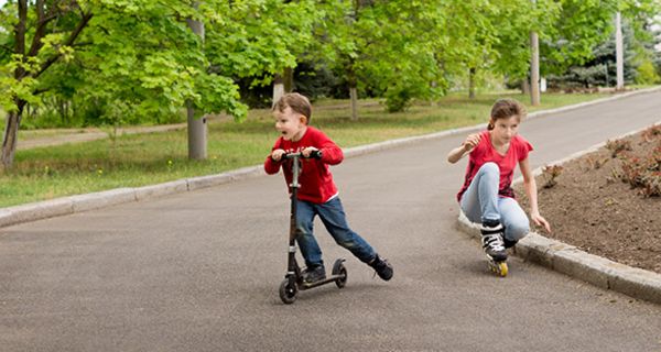 Junge ca. 5, auf Tretroller, Mädchen, ca. 9/10, auf Rollerblades auf Straße in Kurve