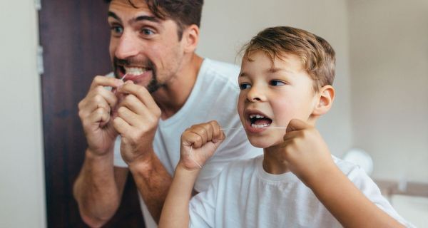 Vater und Sohn, stehen vor dem Spiegel und nutzen Zahnseide.