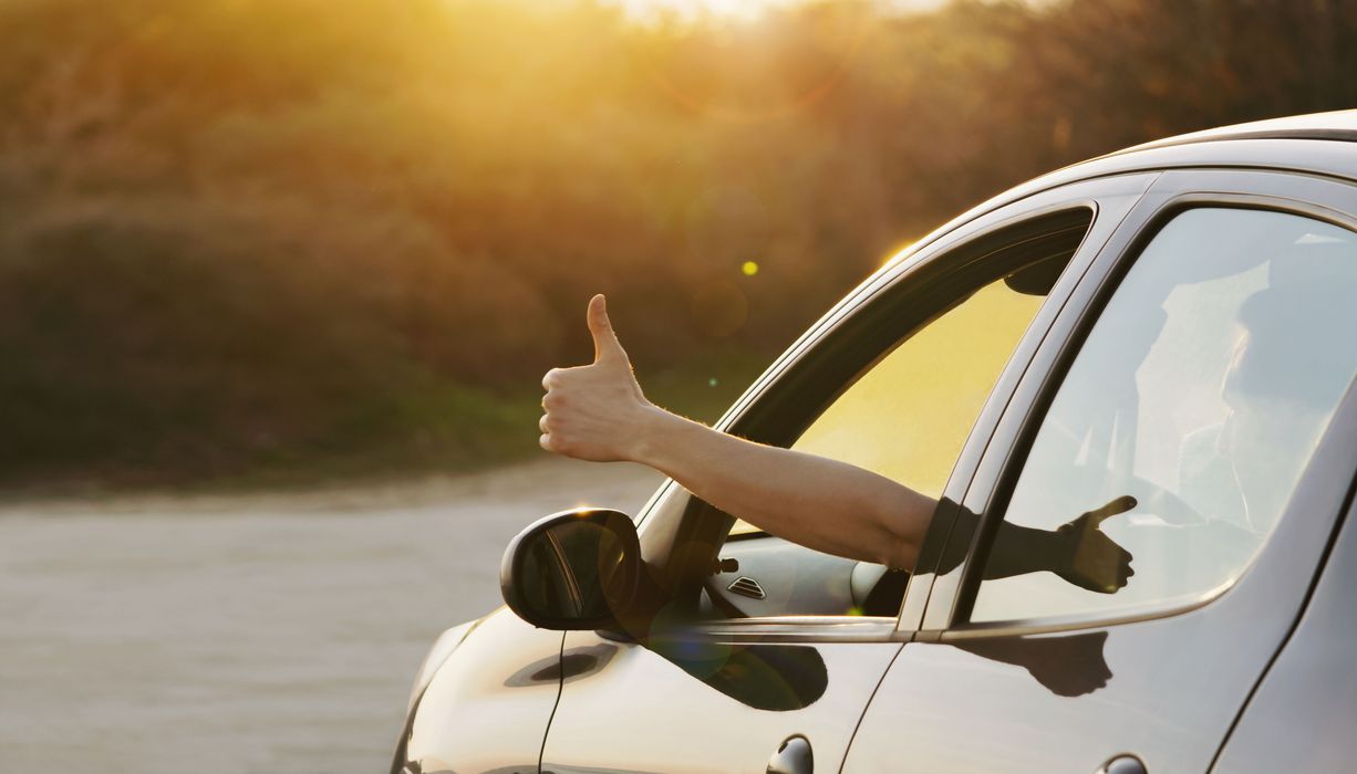 Aus einem Autofenster signalisiert eine Hand: Daumen hoch. 