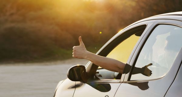 Aus einem Autofenster signalisiert eine Hand: Daumen hoch. 