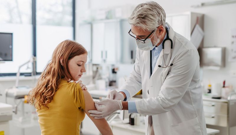 Ein Arzt impft eine Jugendliche.