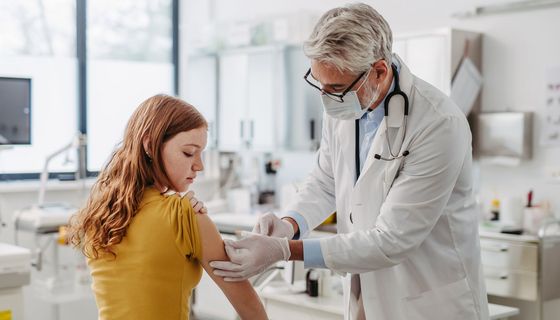 Ein Arzt impft eine Jugendliche.