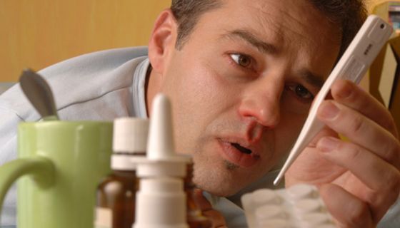 Mann mit Grippe liegt im Bett und liest Fieberthermometer ab