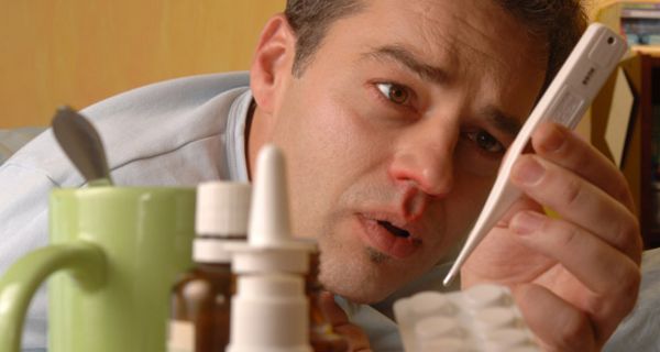 Mann mit Grippe liegt im Bett und liest Fieberthermometer ab
