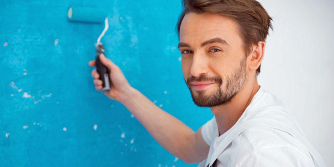 Junger Mann in weißem Overall streicht eine Wand blau an