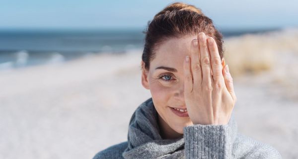 Frau am Strand, hält ein Auge mit einer Hand zu.