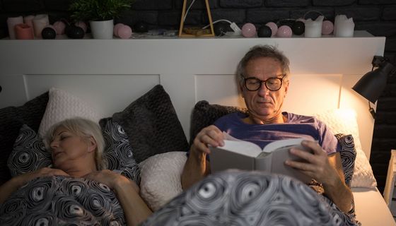 Senioren-Paar liegt im Bett, Mann ist noch wach und liest.