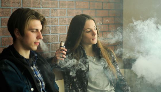 Zwei Jugendliche – Mädchen und Junge – rauchen zusammen E-Zigaretten.