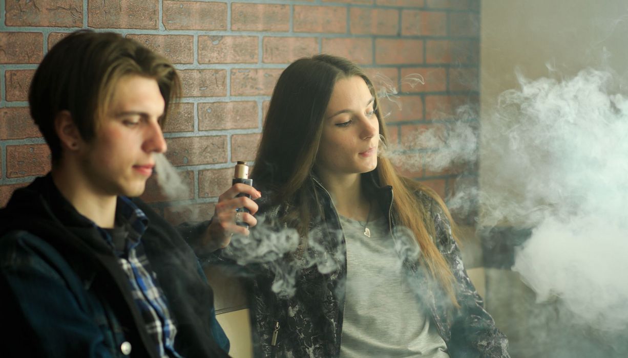 Zwei Jugendliche – Mädchen und Junge – rauchen zusammen E-Zigaretten.