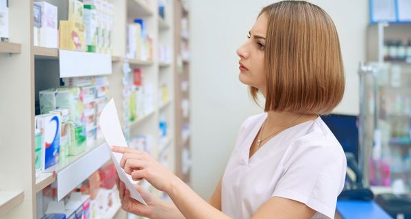 Apothekerin sucht nach einem Medikament im Regal.