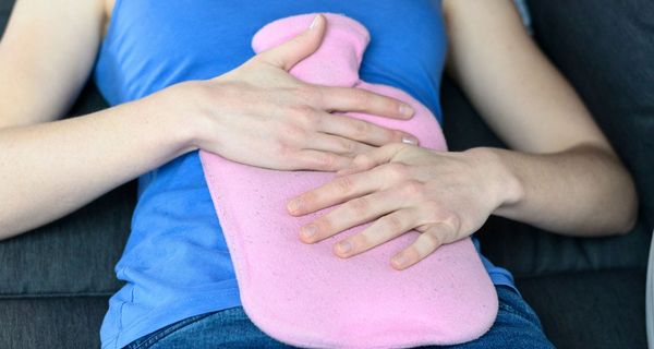 Frau liegt auf dem Rücken mit einer Wärmflasche auf dem Bauch.