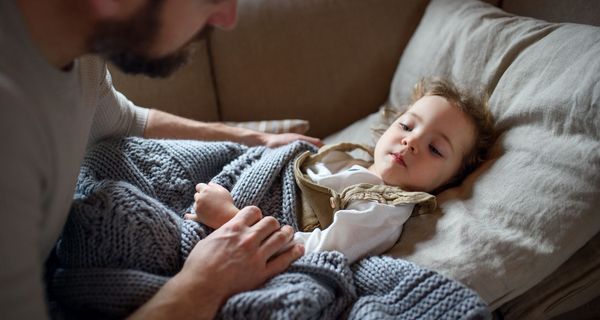 Kind, liegt im Bett, Papa sitzt daneben.