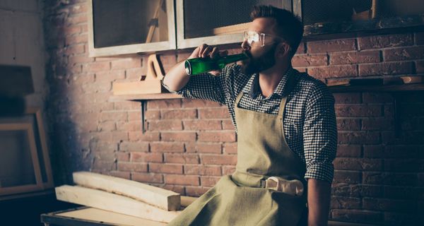 Handwerker, sitzt auf Arbeitsbank und trinkt ein Bier.