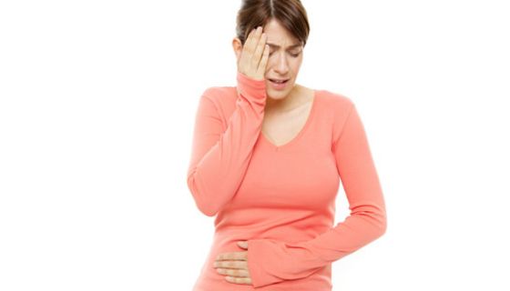 Junge Frau fasst sich vor Schmerzen an den Bauch und an die Schläfe