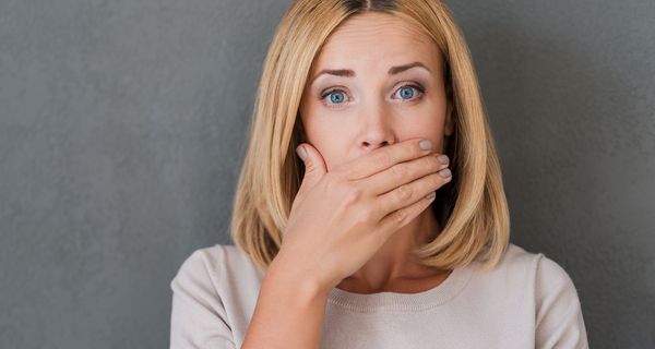 Blonde Frau, hält sich die Hand vor den Mund.