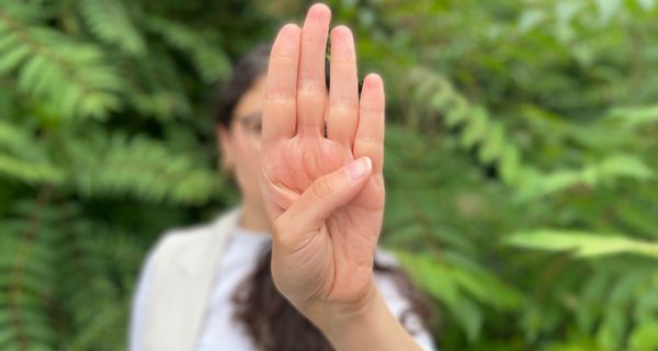 Junge Frau zeigt die Handfläche und streckt den Daumen über die Handfläche auf die gegenüberliegende Seite. 