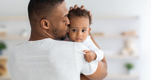 Vater, hält sein Baby auf dem Arm und küsst es auf die Stirn.