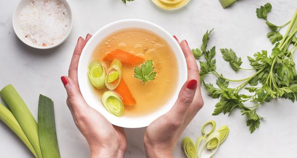 Frau, hält eine Schüssel mit Gemüsesuppe zwischen den Händen.