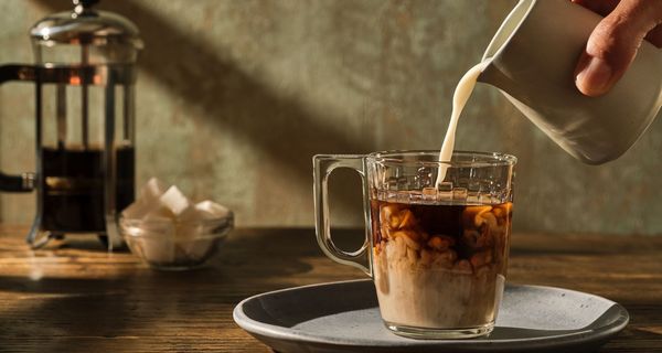 Mann, gießt Milch in einen Kaffee.