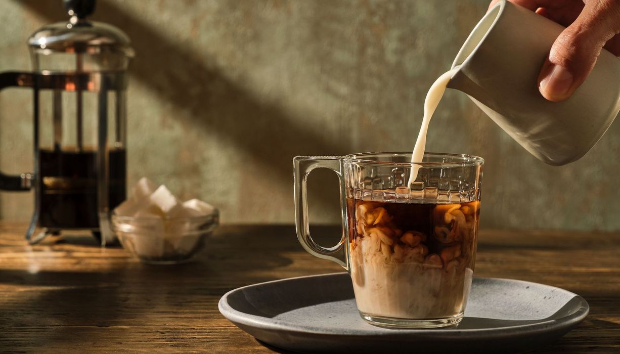 Mann, gießt Milch in einen Kaffee.