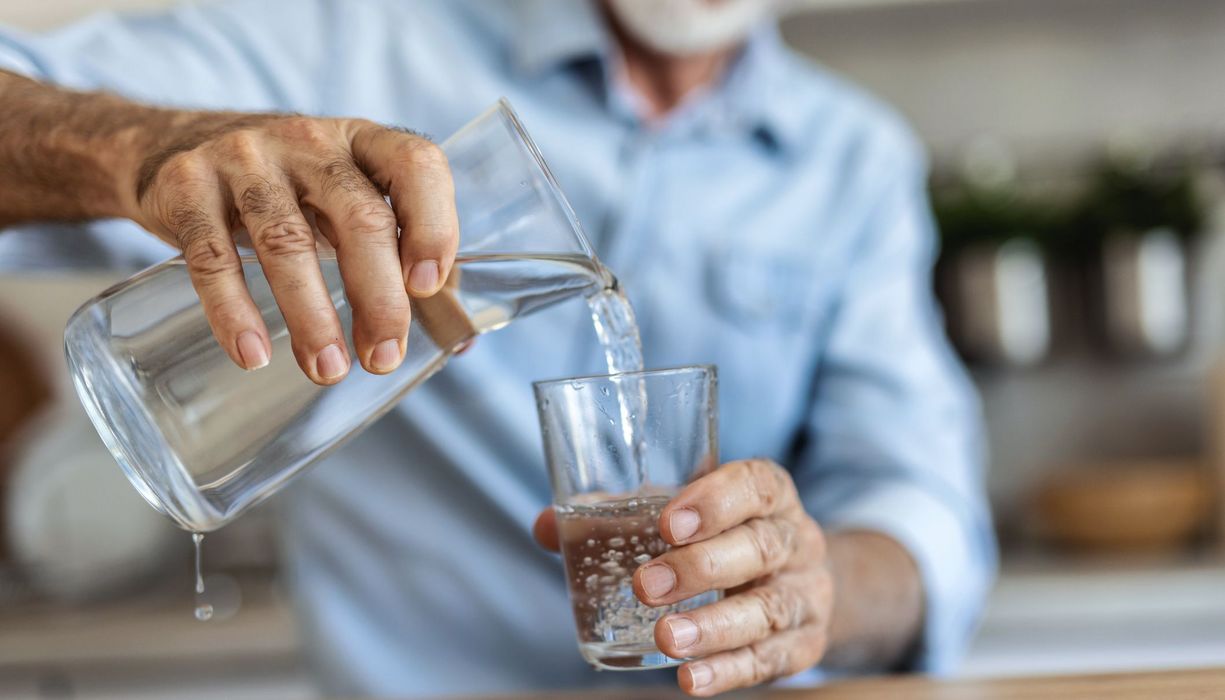 Mann, gießt sich Wasser aus einer Karaffe ein.
