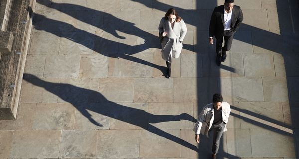 Menschen gehen in der Stadt mit langen Schatten.
