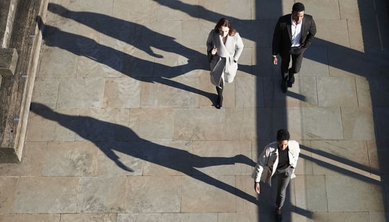 Menschen gehen in der Stadt mit langen Schatten.