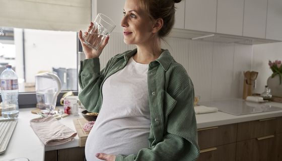 Schwangere Frau trinkt ein Glas Wasser in der Küche.