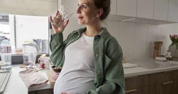 Schwangere Frau trinkt ein Glas Wasser in der Küche.