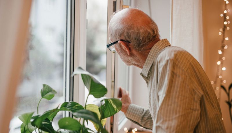 Älterer Mann, steht am Fenster.