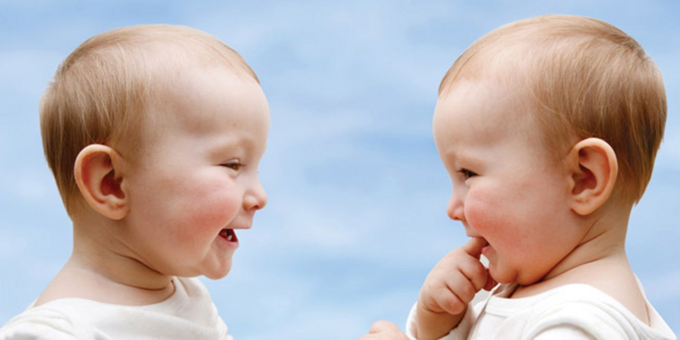 Zwei Babys sitzen einander gegenüber und lachen