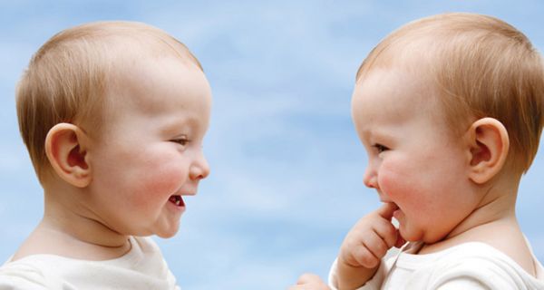 Zwei Babys sitzen einander gegenüber und lachen