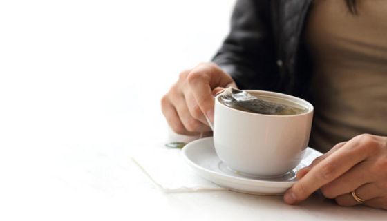 Frauenhände umfassen eine weiße Teetasse mit einem Teebeutel darin