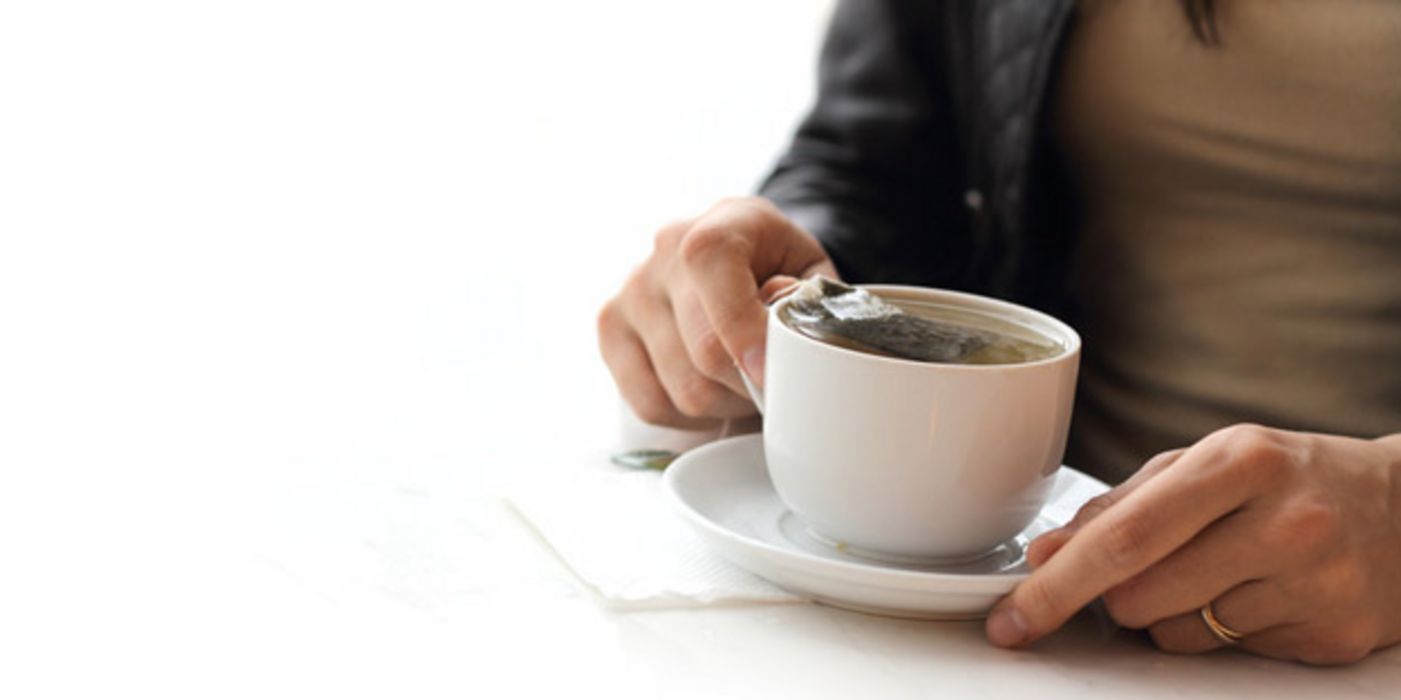 Frauenhände umfassen eine weiße Teetasse mit einem Teebeutel darin