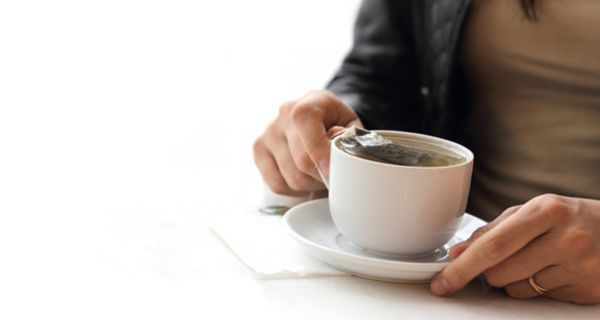 Frauenhände umfassen eine weiße Teetasse mit einem Teebeutel darin